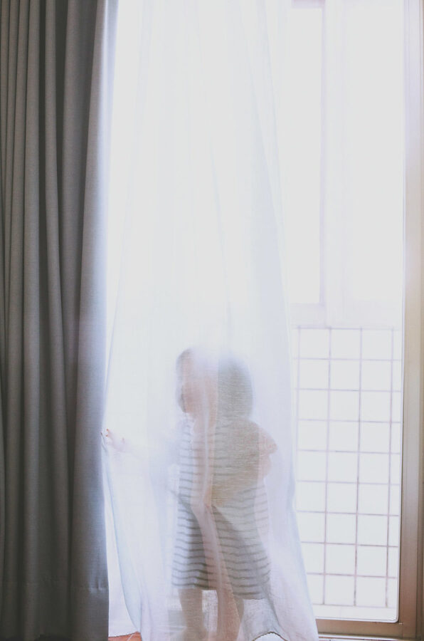 小女孩藏在白色窗簾後，光線柔和，畫面夢幻，台北親子寫真