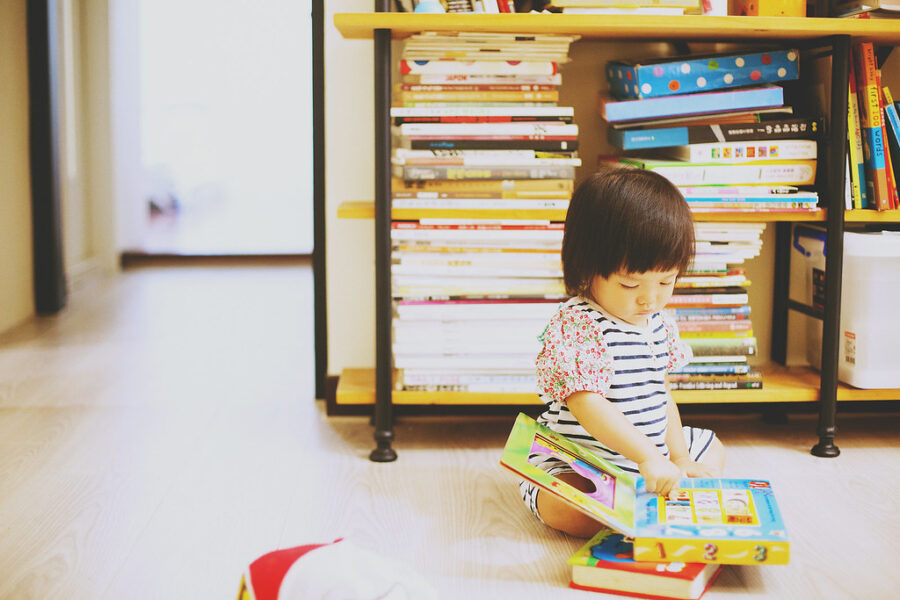 小女孩坐在書架前翻閱繪本，陽光灑進房間，台北親子寫真