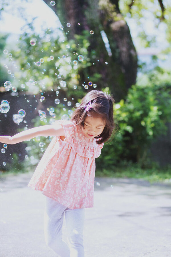 小女孩在陽光下追逐泡泡，笑著揮手，畫面充滿童趣，台北親子寫真