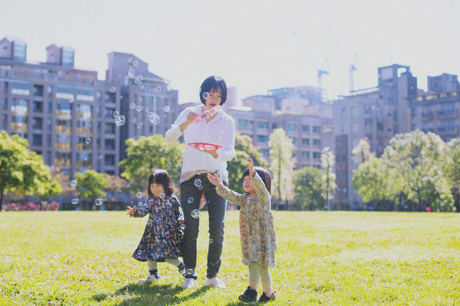 台北親子寫真，媽媽在草地上吹泡泡，兩個孩子伸手追逐泡泡